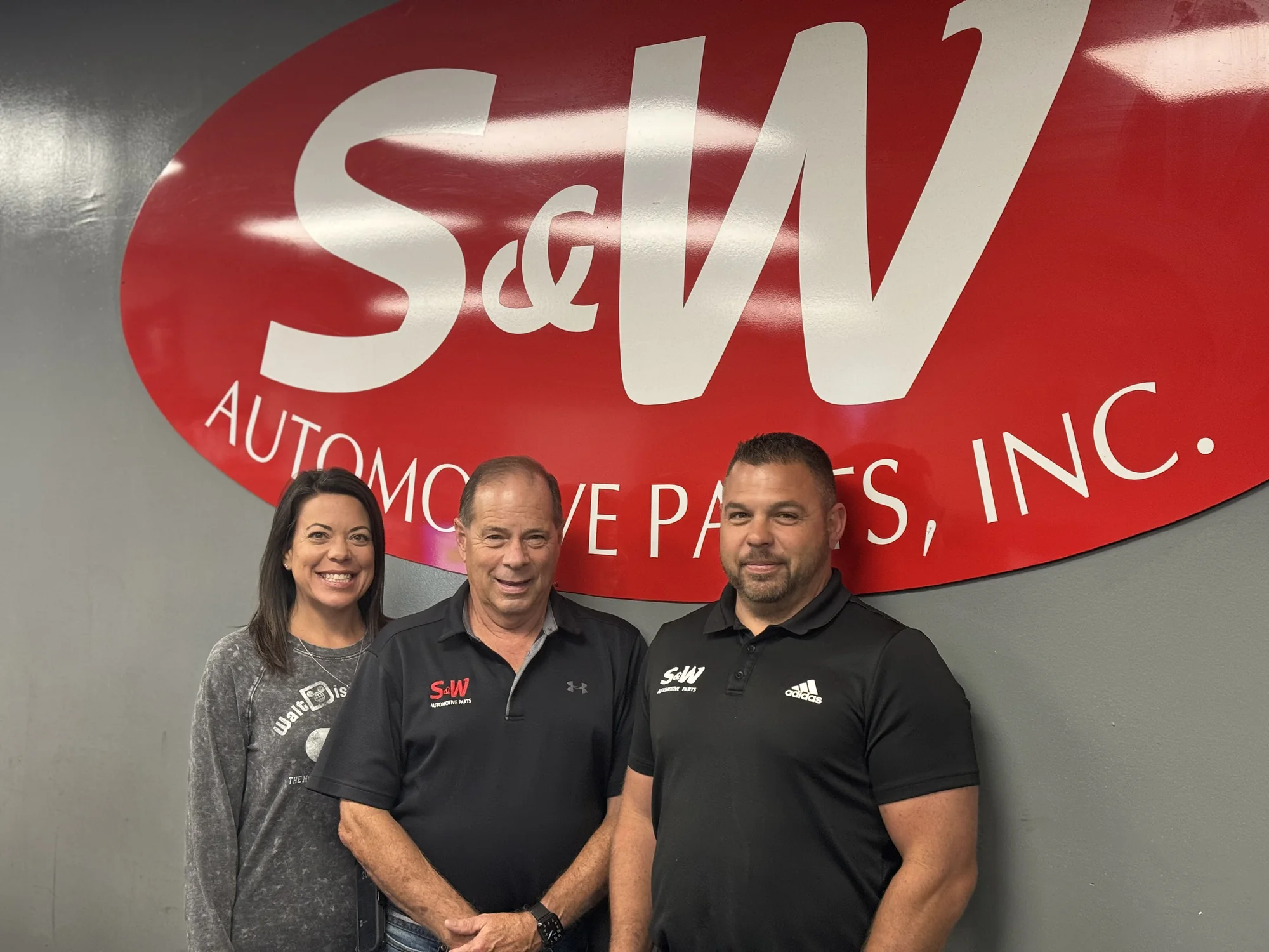 Owners of S&W Automotive Parts standing beneath the company logo